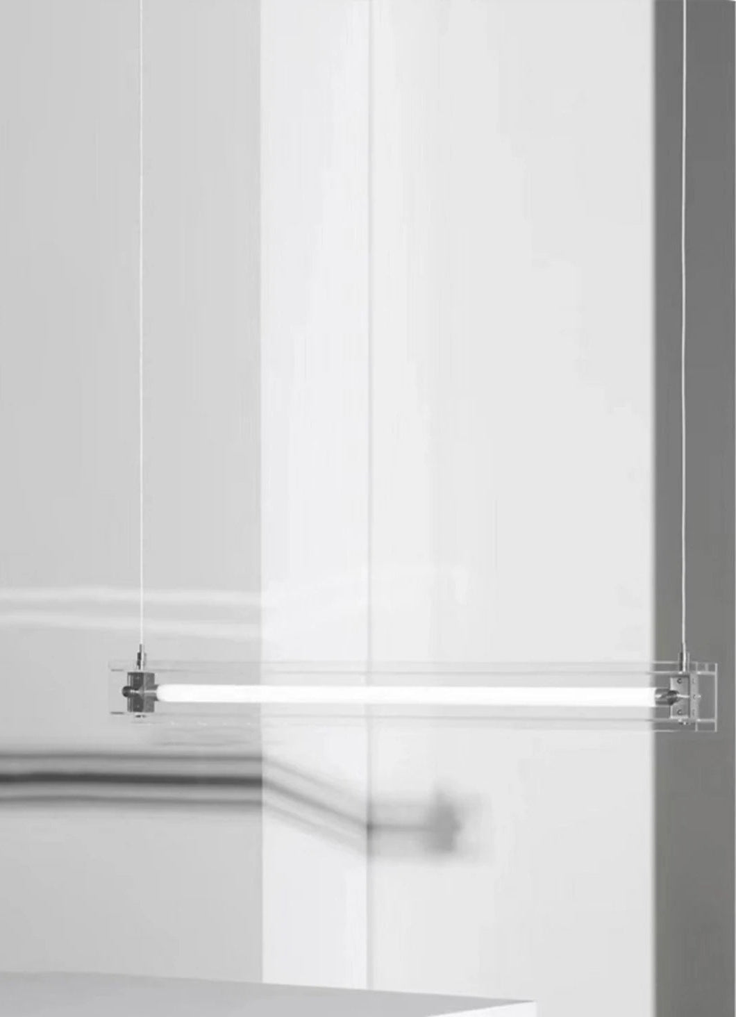 A modern, sleek linear glass pendant light with stainless steel accents, suspended over a counter, dispersing a warm glow.
