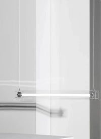 A modern, sleek linear glass pendant light with stainless steel accents, suspended over a counter, dispersing a warm glow.
