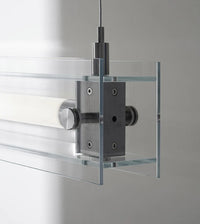 A modern, sleek linear glass pendant light with stainless steel accents, suspended over a counter, dispersing a warm glow.