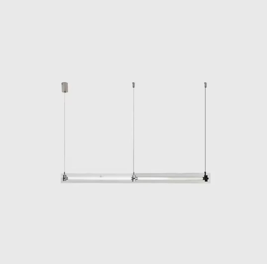 A modern, sleek linear glass pendant light with stainless steel accents, suspended over a counter, dispersing a warm glow.