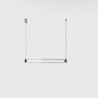 A modern, sleek linear glass pendant light with stainless steel accents, suspended over a counter, dispersing a warm glow.
