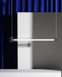 A modern, sleek linear glass pendant light with stainless steel accents, suspended over a counter, dispersing a warm glow.